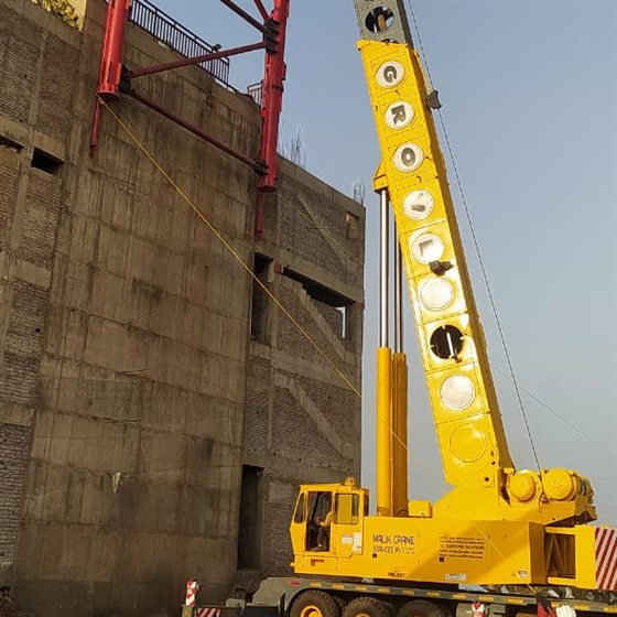 Grove truck crane with boom extended, lifting a red steel gantry at a construction site