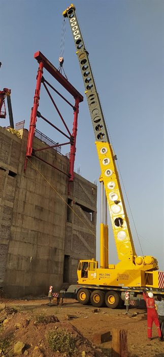 Grove truck crane lifting a red steel gantry at a construction site